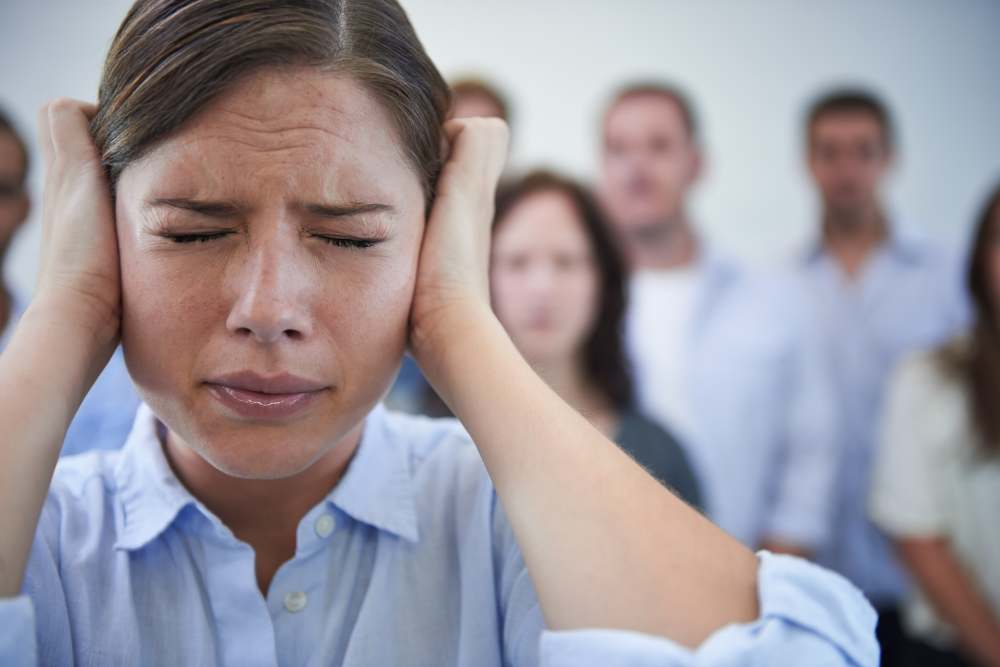 A woman looking stressed and overwhelmed as her bosses watch her, representing the negative impact of imbalanced employee surveillance on mental health and well-being in the workplace.