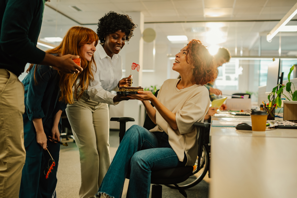 Team members celebrate their colleague's achievements with a gesture of appreciation, offering cake as recognition for her hard work and contributions to the team's success.