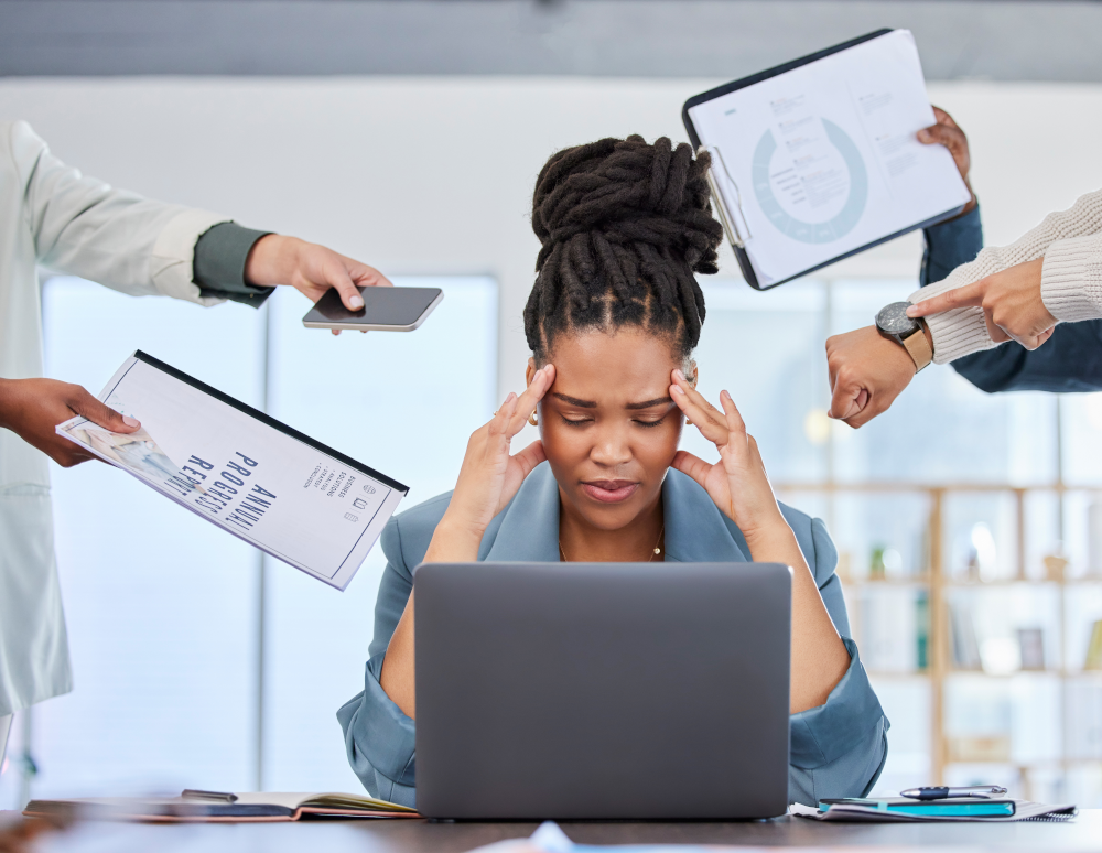 Image of a woman at her desk looking stressed and overwhelmed, representing workplace stress and burnout, highlighting the importance of employee well-being and mental health programs.