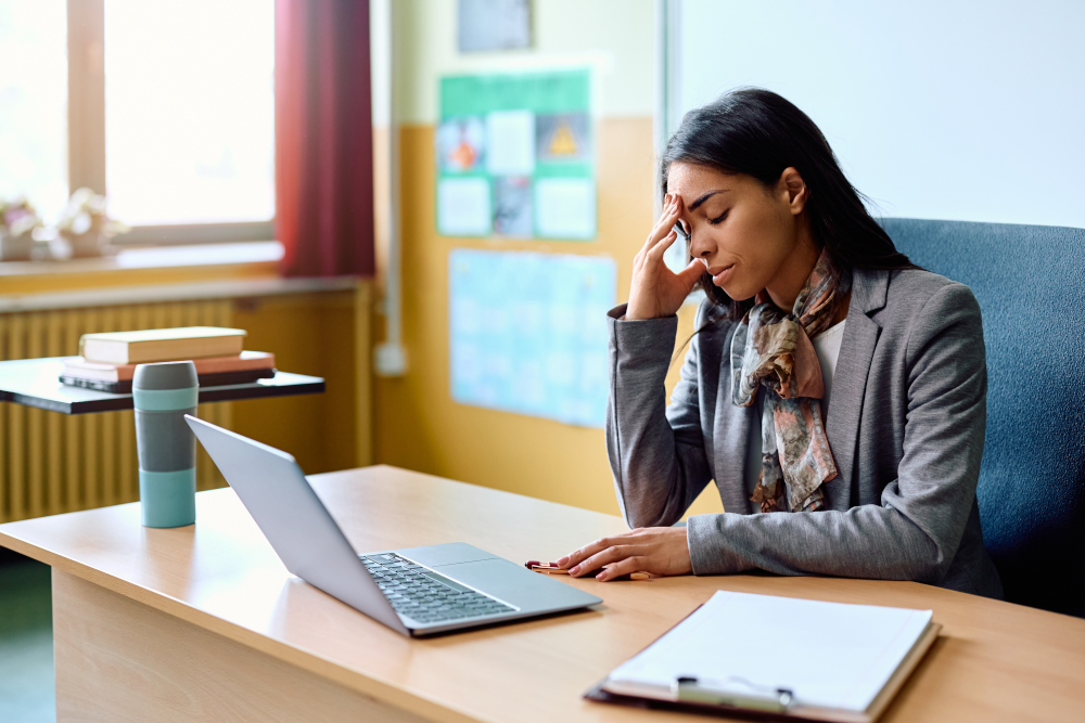 Image of a stressed teacher in a classroom setting, reflecting the challenges faced by public K-12 teachers, including high stress levels, concerns about student academic performance and behavior, and overwhelming workload.